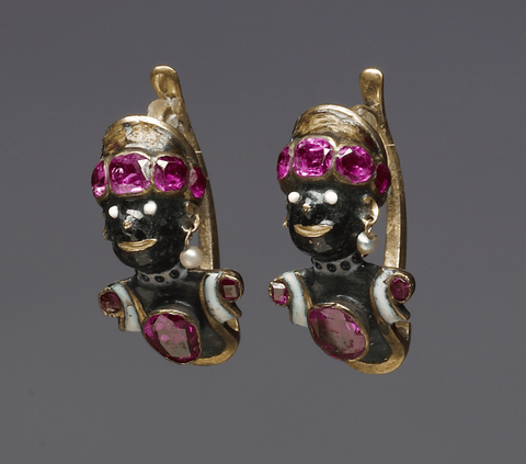 The focal point of this pair of earrings rests upon the intricately designed heads resembling Africans. These figures sport vibrant green headgear adorned with three ruby pastes. 