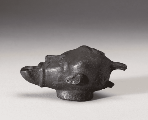 A blackened bronze oil lamp in the shape of a man's head, the open mouth is where the flame would come out. 
