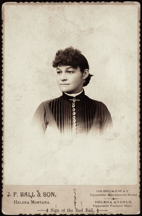 Head and shoulders portrait of an unidentified African American woman with brooch above buttoned shirt and wearing earings.