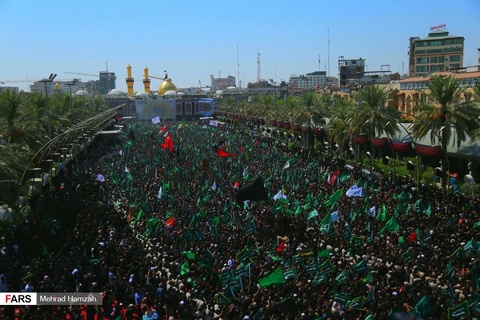 A palm-lined street, completely full of people wearing black clothing and waving green flags. The gold minarets and dome of a mosque can be seen in the distance