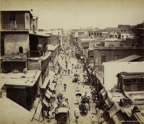 A wide street, open air model of bazaar with sufficient space for horse carriages, and not too crowded (at least at the time the photo was taken). It’s either a model of stark contrast in Indian bazaars to the ‘traditional’ Islamic markets, or an example of transformation and industrialization at play, perhaps due to English influence. 

