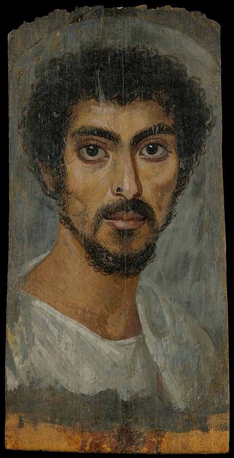 A portrait of a man with dark curly hair, facial hair, and large round eyes. He wears a white garment. 