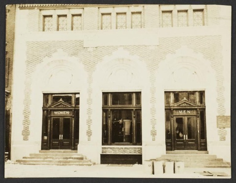 A photograph of the Montrose Avenue Bath House. There are two separate entrances with stairs leading to either. Above the double doors on the left it reads: WOMEN and on the right: MEN.