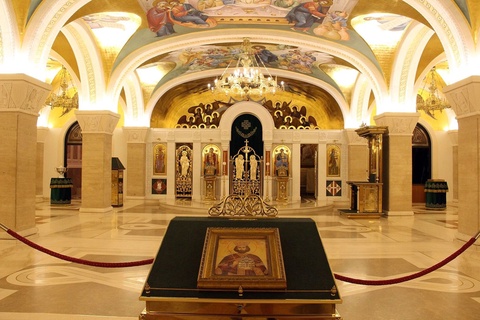 The interior of a gilded church with an icon on a stand and frescoes on the ceiling vaults.