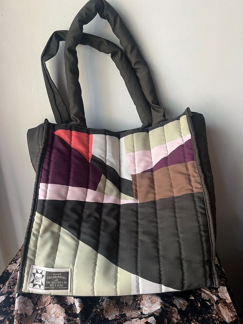 A colorful quilted tote bag sitting on patterned fabric.