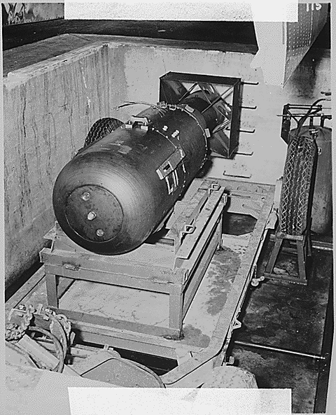 A large metal capsule sits on a metal frame in a cement pit in this black and white photograph.