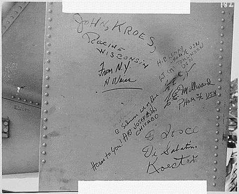 A close-up of signatures and messages written in black ink on a sheet of metal. The names include “John Kroes” and “H.P. Lemay.”