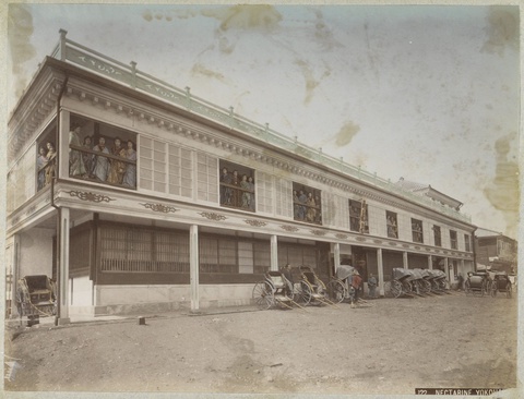 A 19th century, albumen print of the Nectarine brothel. Sex workers stand in the second-floor window. Rickshaw drivers stand beside their vehicles on the street. 