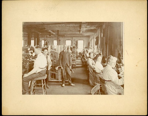 A sepia-toned photo of a textile factory floor focuses on an older male manager wearing a suit.