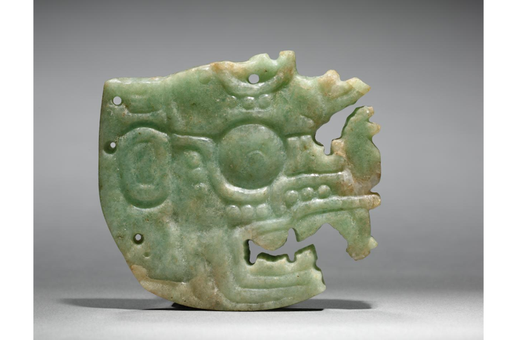 A Jadeite-albitite crown ornament carved in Maya style. The ornament features a deity in profile with a bulging eye.