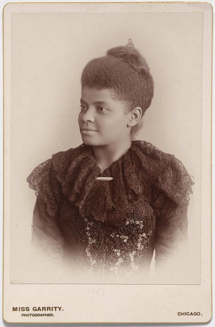 A sepia-toned photograph of a woman looking off-camera in a three-quarter pose. Her hair is in an updo and she is wearing a dark lace garment. 