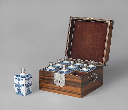 A set of nine porcelain bottles with blue decoration. Eight are placed in a gridded wooden box with silver details.
