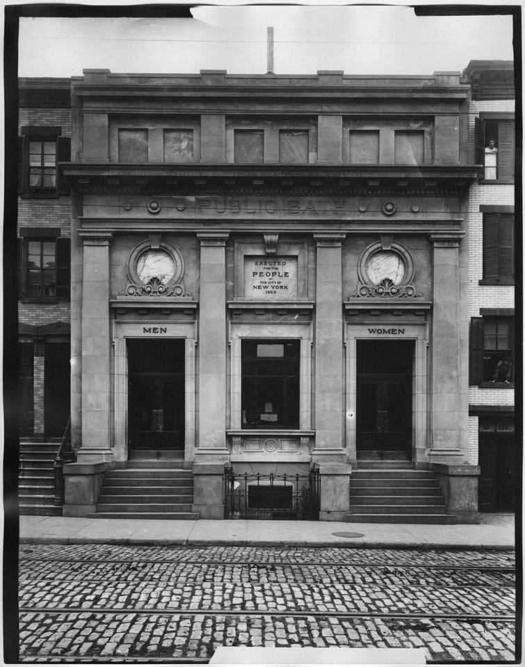 A black and white photograph of an unidentified building facade in Manhattan. The entablature reads: PUBLIC BATH. Underneath this in a square portal it reads: ERECTED FOR THE PEOPLE OF THE CITY OF NEW YORK 1903.