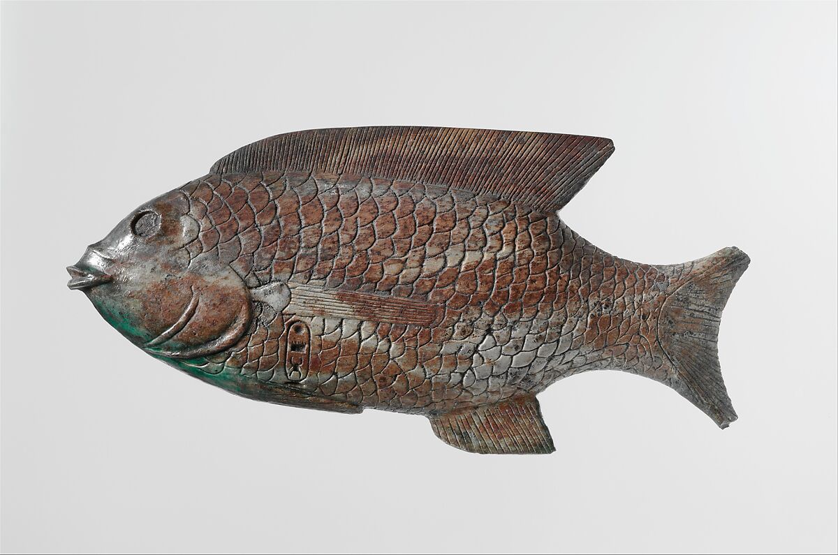 A New Kingdom cosmetic dish shaped like a bolti fish. The fish is incised with scales and detailing on its fins. A cartouche near its gills is inscribed with a throne name.