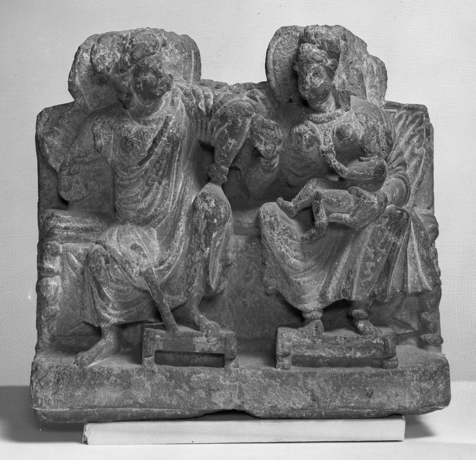 Unknown, <i>Small Relief of Hariti</i>, late 2nd–3rd century. Brooklyn Museum. This fragment of a relief sculpture in black slate depicts goddess Hariti on the right, holding a child next to a male deity, either Panchika or Kubera.