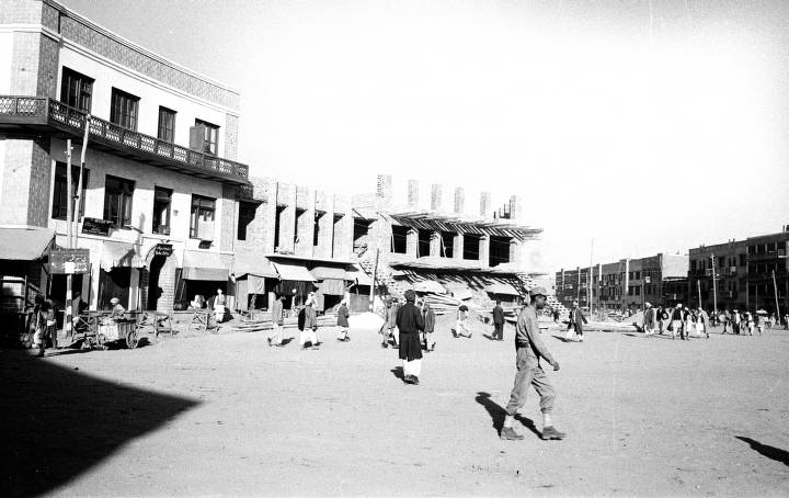 A black and white photograph taken facing one side of a street in Kabul, Afghanistan. The buildings are newly constructed and people pass by on the side of the roadway.