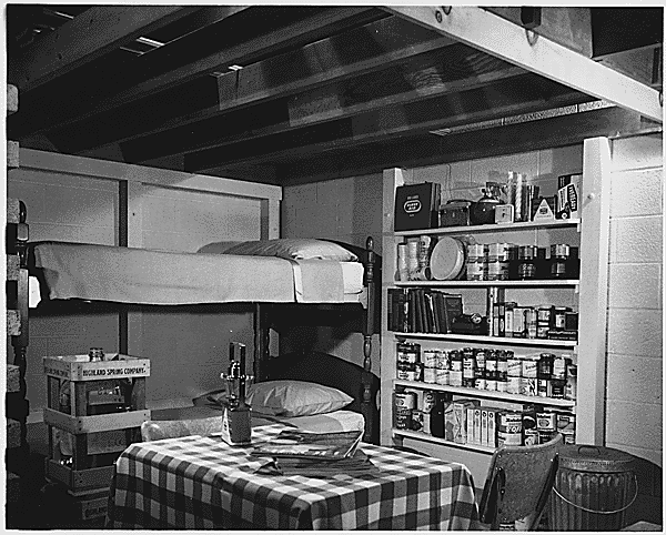 A domestic scene consisting of a set of neatly made bunkbeds, open shelves, and a table and chairs. Visible roof beams and what look like cinderblock walls make the scene appear to be underground. 